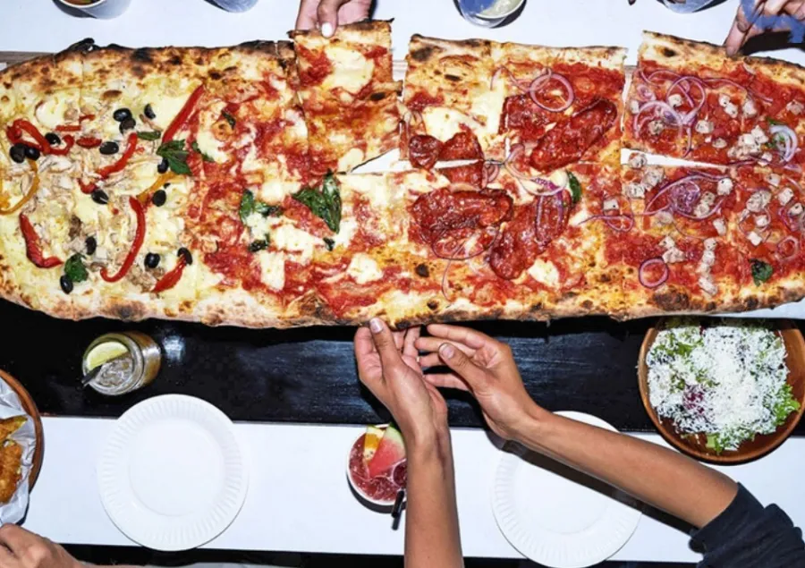 A long shared pizza on a table at a community gathering