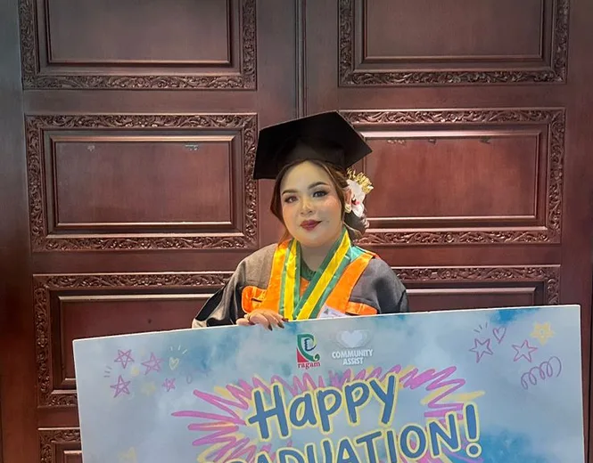 Ni Putu Chintya Pratiwi in cap and gown holding a Happy Graduation sign