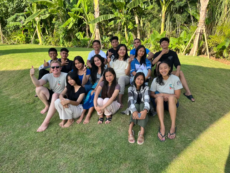 Students and mentors sitting together on the grass at a community day.